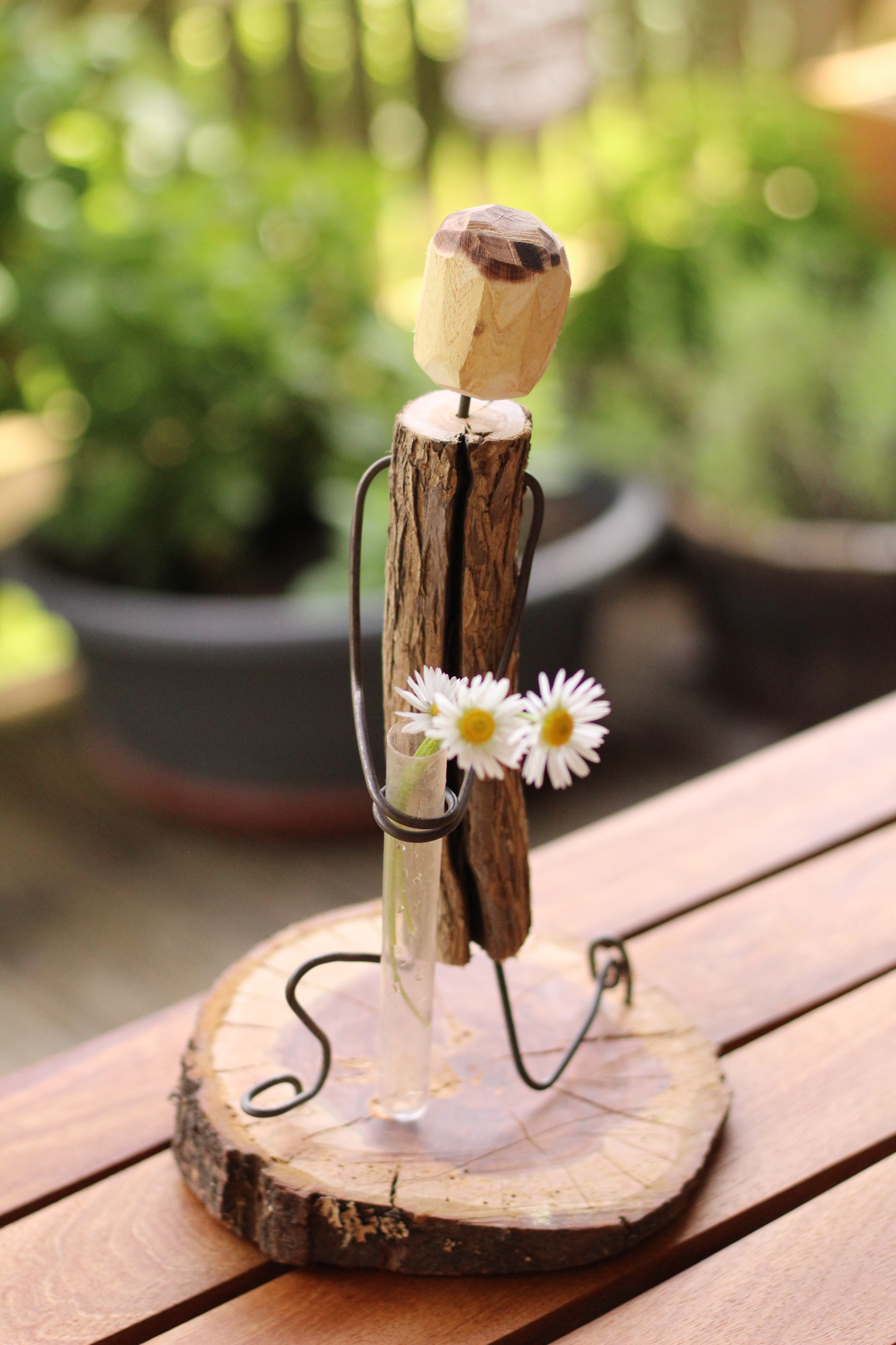 Knieendes Holzmännchen mit Gänseblümchen in der Hand